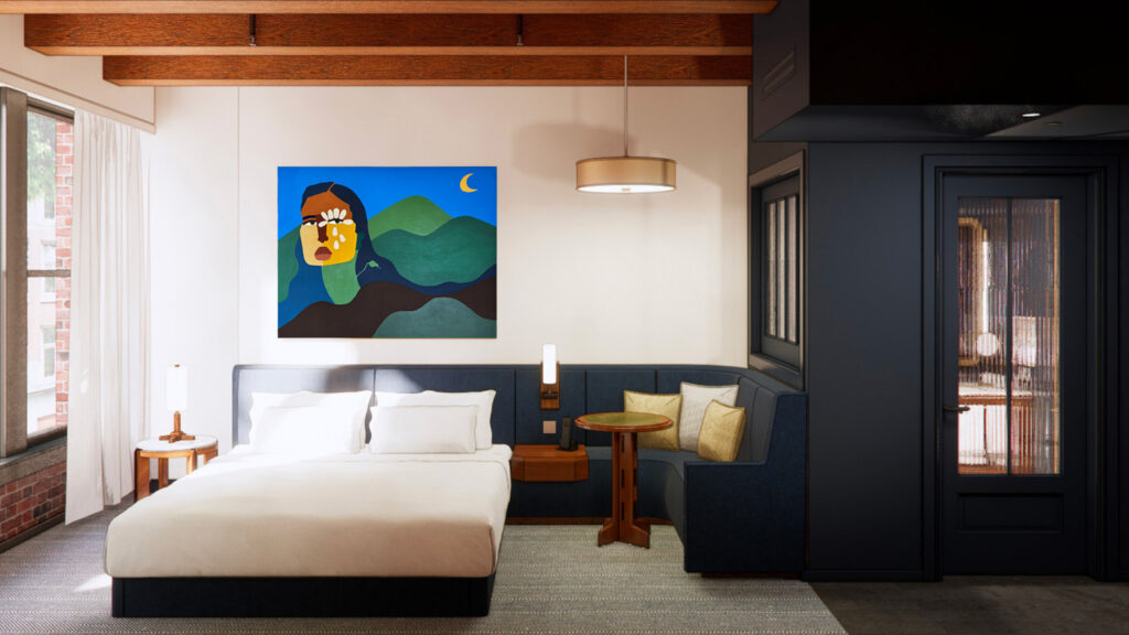 Interior of a King Room at Populus Seattle featuring a plush king-size bed with white linens, a cozy built-in navy banquette with a round wood table, large abstract artwork of a woman's face emerging from the ground set above the headboard, exposed ceiling beams, and a mix of modern and natural textures throughout the space.