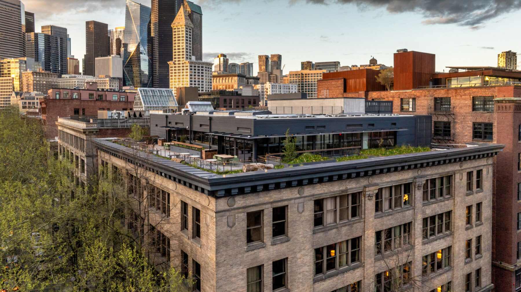 Aerial view of the rooftop at Populus Seattle, featuring a modern black addition with greenery above a historic brick building, framed by the downtown skyline.