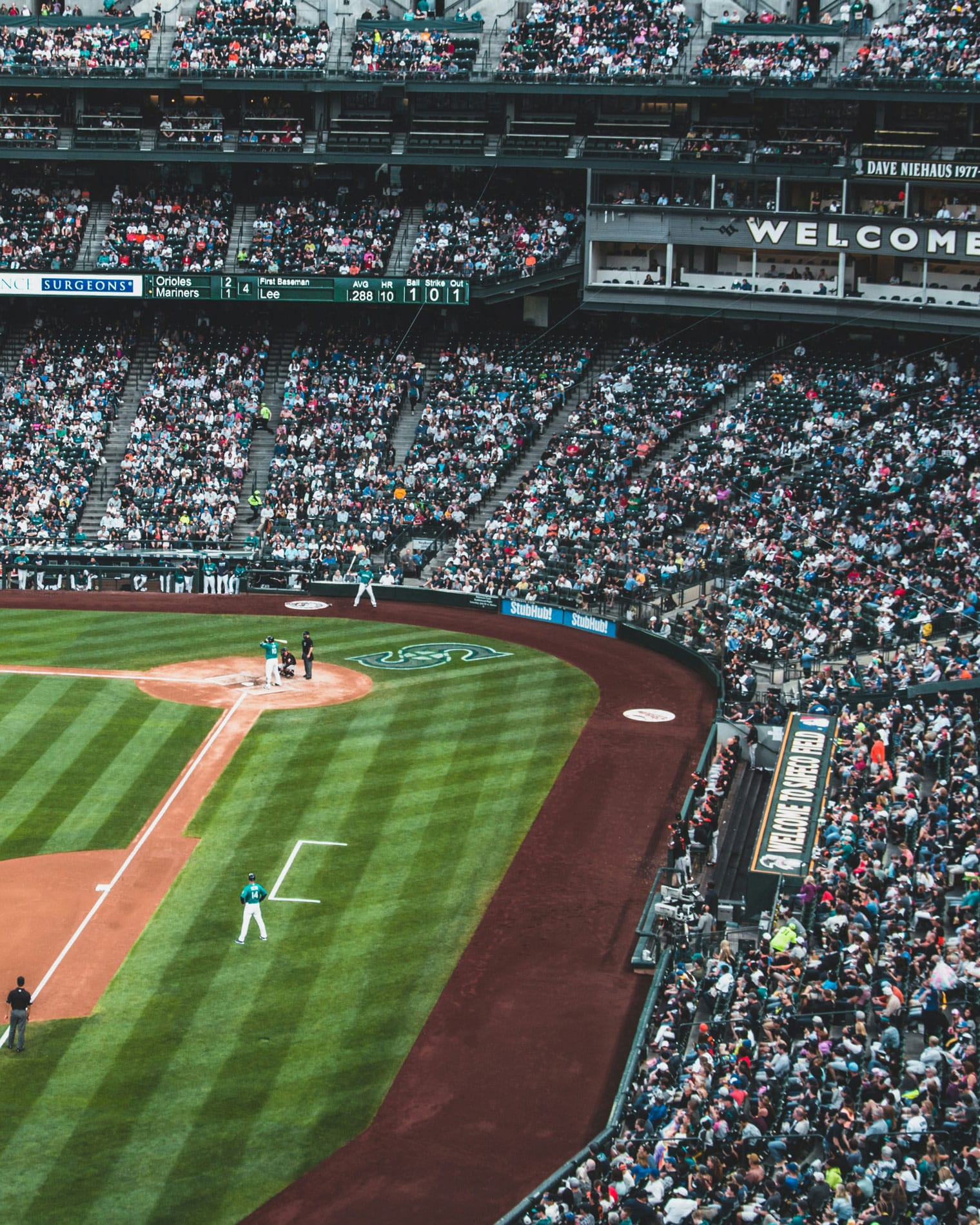 A packed stadium during a Seattle Mariners baseball game at T-Mobile Park, showing fans in the stands, players on the field, and the scoreboard above the first baseline.