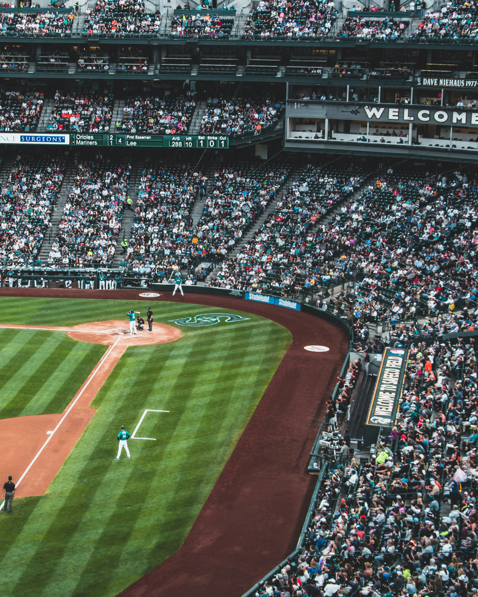A packed stadium during a Seattle Mariners baseball game at T-Mobile Park, showing fans in the stands, players on the field, and the scoreboard above the first baseline.