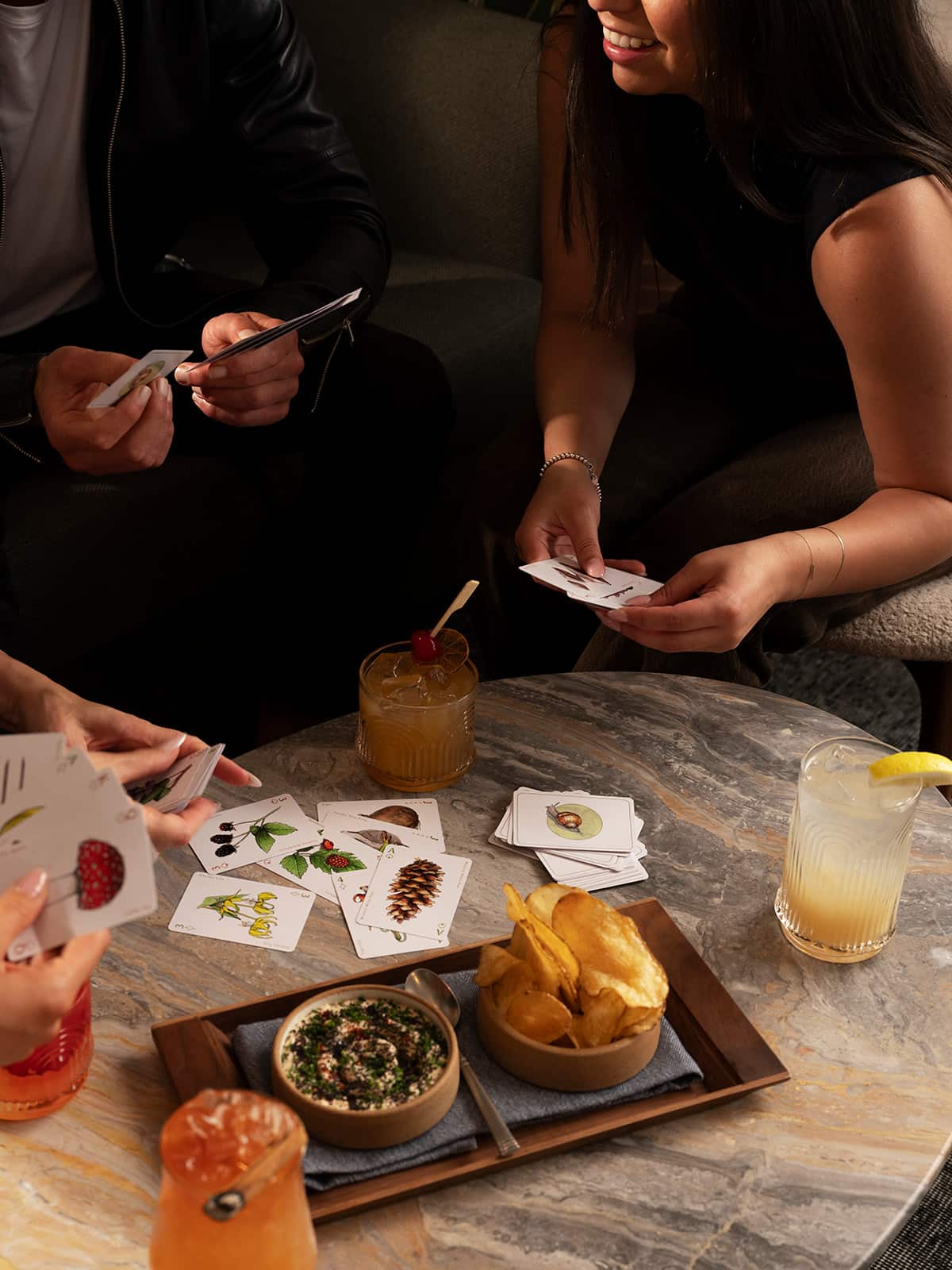 Two women playing cards while sharing small plates and cocktails at the Firn rooftop